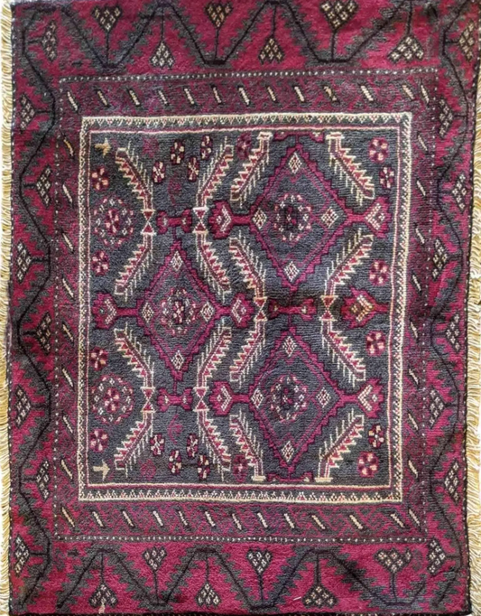A Persian Baluch rug featuring a geometric pattern with deep reds, dark blue, and white colors, indicative of the tree of life design.