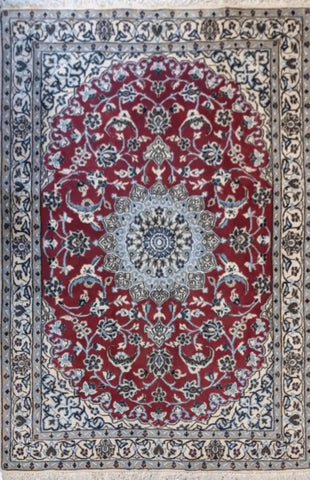 A traditional Persian Nain rug with a red primary color and intricate blue patterns, featuring floral and geometric designs.