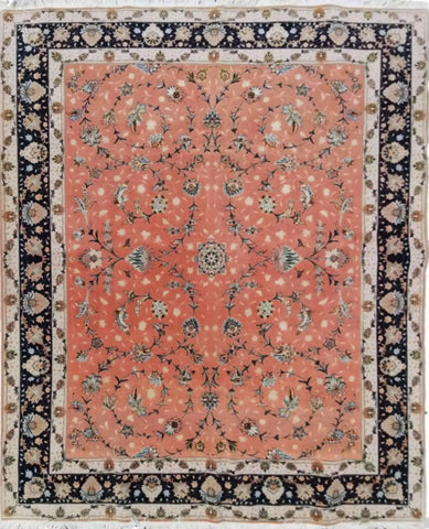 A traditional Tabriz salmon pink wool and silk rug with a geometric and floral pattern, featuring a central medallion and a dark border.