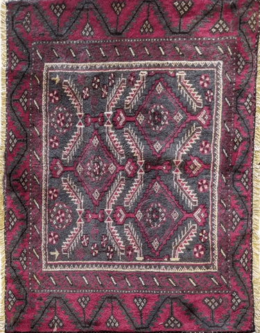 A Persian Baluch rug featuring a geometric pattern with deep reds, dark blue, and white colors, indicative of the tree of life design.